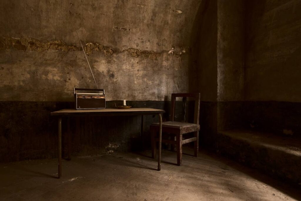 Tafel met stoel en oude Philips radio in stenen gebouw Urbex © Hans Honsbeek